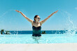 © Westend61 - Mature woman splashing water and having fun in swimming pool at resort