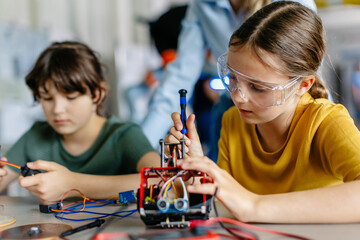 school girls working on circuit board of small robot, building robotic car in after-school robotics 