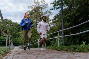 Wall Mural - Man and woman jogging up a hill on a paved path, laughing and enjoying their run together. They are dressed in hoodies and athletic leggings.