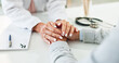 © HockleyM1/peopleimages.com - Doctor, patient and holding hands on desk in consultation room with support, empathy and announcement. Medic, person and care with comfort, diagnosis and helping with healthcare service at hospital