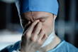 © Seventyfour - Close up portrait of exhausted surgeon rubbing eyes standing in dark operating room