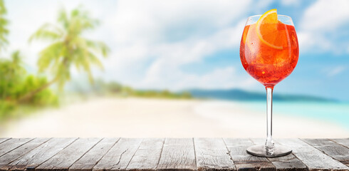 Poster - Glass of Aperol Spritz on a table with a stunning sea and beach background