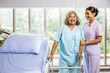 © TeTe Song - Female nurse helping elderly female with walking frame stand up from bed at home. Professional care for disabled patients,  Disable old woman trying to walk with the assistance aid of female doctor
