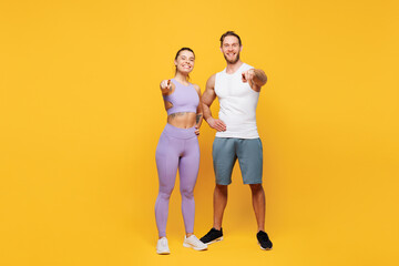 Wall Mural - Full body young strong fitness trainer sporty two man woman wearing blue clothes spend time in home gym point index finger camera on you isolated on plain yellow background. Workout sport fit concept.