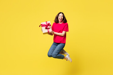 Full body young surprised shocked woman wear pink t-shirt casual clothes jump high hold present box with gift ribbon bow isolated on plain yellow orange background studio portrait. Lifestyle concept.
