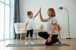 © standret - Well done, doing high five. Young woman with little girl are doing yoga at home