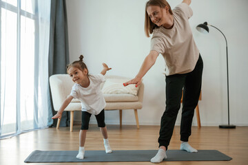 Wall Mural - Focused on the exercise. Young woman with little girl are doing yoga at home