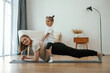 © standret - Kid is sitting on a back of woman. Young mother with little girl are doing yoga at home