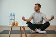 © standret - Bottles of water and apples. Yoga man is sitting on a mat at home