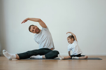 Sticker - Against white wall, stretching. Father with little daughter are doing yoga at home