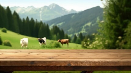 Wall Mural - Wooden table foreground with alpine meadow and cows with mountain backdrop. Rural life and eco-tourism concept. Cow walking and eating grass at animal farm with green mountain and blue sky. AIG35.