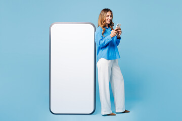 Wall Mural - Full body side view young woman wear shirt casual clothes big huge blank screen mobile cell phone with copy space area use smartphone isolated on plain light blue cyan background. Lifestyle concept.