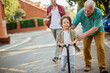 © Geber86 - Father and grandfather teaching young boy to ride a scooter on suburban street