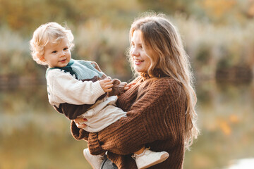 Young mother 24-26 year old holding baby over nature background. Autumn season.