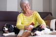 © luciano - Smiling senior woman sitting on sofa with her two Cavalier King Charles dogs cuddling close up. Relaxing time of her spending quality time with her beloved pets beside her