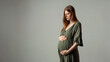 © SFotoz - A pregnant woman in a green dress poses, holding her hands on her belly, standing against a neutral background.