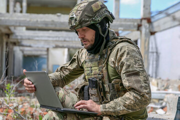 Wall Mural - Military mission. Soldier in uniform using laptop near abandoned building outside