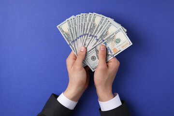 Money exchange. Man holding dollar banknotes on blue background, top view