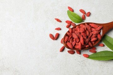 Wall Mural - Dried goji berries, leaves and spoon on light textured table, flat lay. Space for text