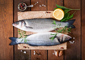 Two raw seabass with spices on an old wooden background.