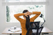 © kenchiro168 - Woman taking a break and stretching at desk in home office.
