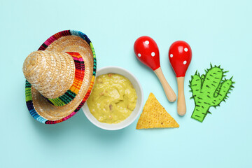 Wall Mural - Mexican sombrero hat, guacamole, nachos chip, maracas and paper cactus on light blue background, flat lay