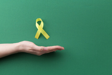 Wall Mural - Woman with yellow awareness ribbon on green background, top view. Space for text