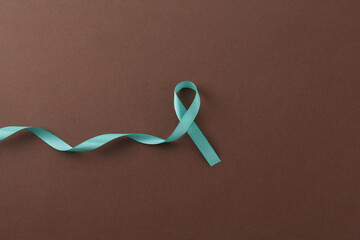 Wall Mural - Turquoise awareness ribbon on brown background, top view. Space for text