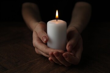 Wall Mural - Woman holding burning candle at wooden table, closeup