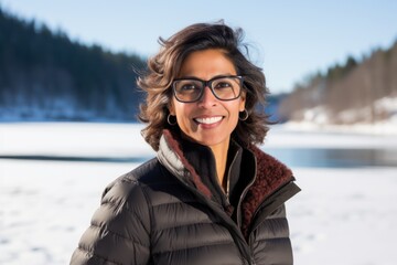 Wall Mural - Portrait of a cheerful indian woman in her 40s donning a classy polo shirt on backdrop of a frozen winter lake