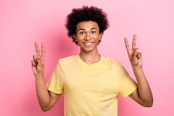 Wall Mural - Photo of cheerful sweet man wear yellow t-shirt smiling showing two v-signs isolated pink color background