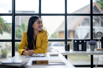 Wall Mural - A woman in a yellow jacket is sitting at a desk with a pen and paper