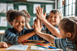 © btiger - Excited children and teacher high-fiving in bright classroom celebrating teamwork and creativity
