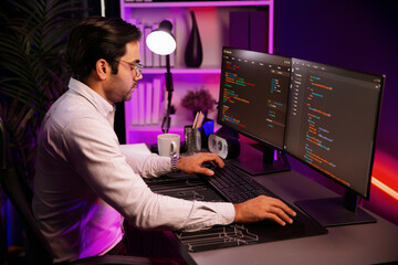 Working smart IT developer analyzing data software development on two pc screen, creating application program updated version online website page system online at neon light cyber office. Surmise.