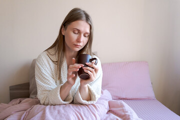 Wall Mural - A woman is sitting on a bed with a cup in her hand