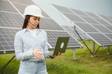 Portrait of young female engineer standing near solar panels. Beautiful female professional in white helmet