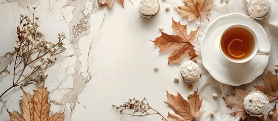 Poster - A scene set for fall: a cozy kitchen table with a delicious cup of tea and cake, surrounded by dried maple leaves and beech, against a white countertop with copy space image.