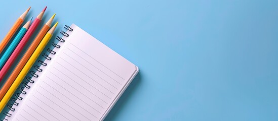 Aufkleber - A bird's eye view of an open notepad and colorful pencils on a blue backdrop, providing ample copy space image.