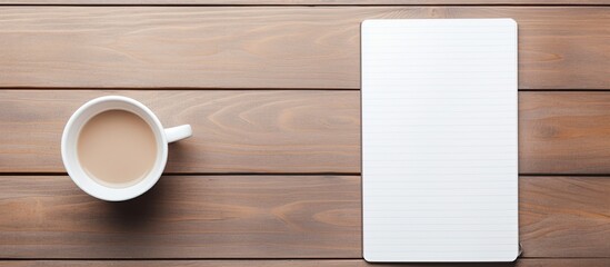 Poster - Aerial view of a wooden desk featuring a blank white smartphone, a coffee cup, a pen, and a spiral notepad with copy space image available.