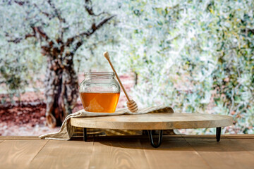 Sticker - Jar of honey on wooden table top with blur nature with green meadow of grass and flowers and trees. Natural field background and place for advertising products.