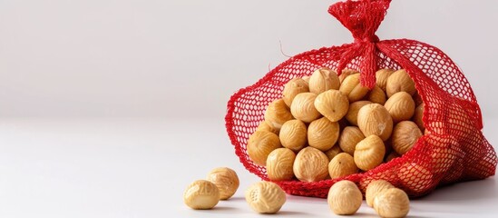 Poster - Macadamia nuts are presented in a red mesh bag set against a white backdrop with copy space image.