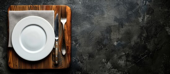 Aufkleber - Top view of an old wooden board with a white plate, fork, and knife on a dark background providing copy space image.