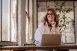© sepy - A woman with blond hair sitting at desk and using her laptop at home