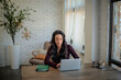 © sepy - African-american woman sitting at desk and home and using her laptop for work