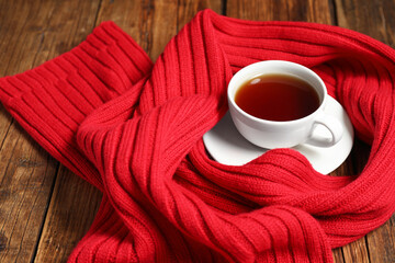 Wall Mural - Red knitted scarf and tea on wooden table, closeup