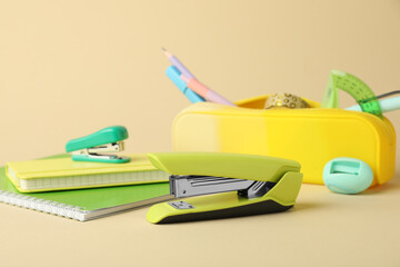 Wall Mural - Green stapler and other stationery on beige background, closeup