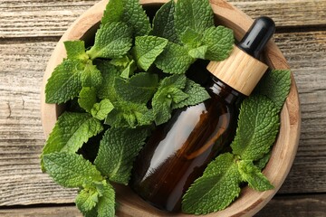 Wall Mural - Bottle of mint essential oil and fresh leaves on wooden table, top view