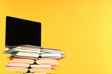 Wall Mural - Stack of colorful books and laptop on yellow background, space for text