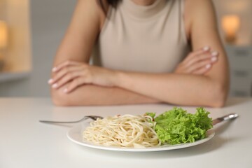 Wall Mural - Eating disorder. Woman at white table with spaghetti and cutlery, selective focus