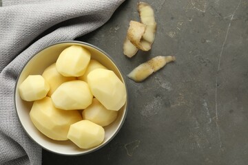Canvas Print - Fresh raw potatoes in bowl and peels on grey table, top view. Space for text